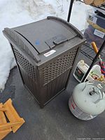 Full view of Suncast brown resin deck box standing upright on driveway