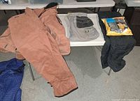 Lot overview showing brown overalls, grey CAT pants, packaged rain suit, black coat