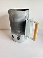 Side view of galvanized steel charcoal chimney starter showing wooden handle and draft holes