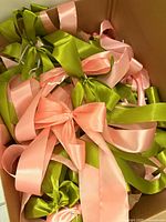 Box containing numerous pink and green satin ribbons tied into bows