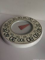 Angled top view displaying round dial, numerals and red pointer