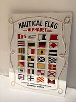 Front of embossed metal sign showing nautical flag alphabet graphics and text