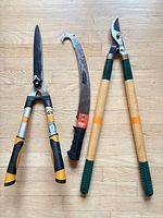 Hedge shears, pruning saw and bypass loppers displayed side by side on wood floor