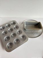 Round pizza pan, 12-cup muffin pan, rectangular loaf pan laid on white surface