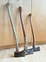 Three wooden-handled axes standing against cabinet