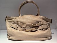 Front view of Brunello Cucinelli beige leather handbag showing overall shape, handles and front pocket