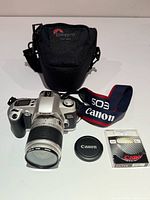 Full lot showing camera with lens, lens cap, filter case, strap, Lowepro bag