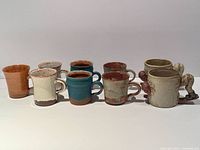 Eight of nine stoneware mugs displayed, assorted glazes and ski novelty mugs visible