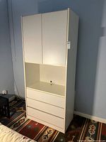 Front view of white shelving unit showing two-door upper cabinet, open shelf, three drawers