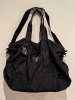 Front view of black nylon Prada duffle with handles and shoulder strap visible