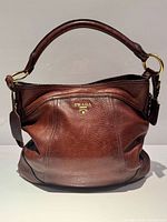 Front view of brown Prada Cervo Antik hobo showing logo, pebbled leather and gold hardware