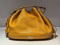 Front view of mustard yellow Prada bucket bag showing pebbled leather and logo plaque