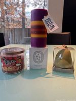 Front view of Pumpkin Apple jar candle, Ambre boxed candle with striped pillar on top, pear candle in clear box