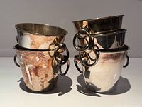 Five silver-plated wine coolers stacked, showing ring handles and finish
