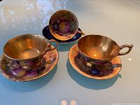 Three signed Aynsley Orchard Fruit tea cup and saucer sets on tabletop