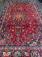 Full view of Persian Mashhad rug showing red field, navy border and overall condition