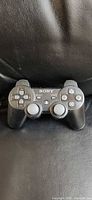 Front view of black Sony DualShock 3 controller on leather seat