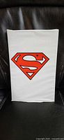 Front view of sealed white polybag with red Superman shield logo