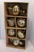 Six gold oversized ornaments in cardboard divider box