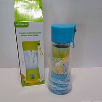 Blue portable rechargeable blender wrapped in protective film beside its retail box