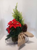 Front view of wicker sleigh arrangement showing poinsettias, greenery, pinecone and burlap bow