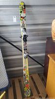 Full view of skis standing vertical showing graphics and bindings
