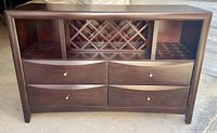 Front view of dark brown sideboard showing four drawers, center wine rack, open side shelves