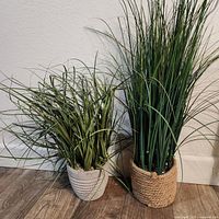 Both faux grass plants side by side showing size difference and pots