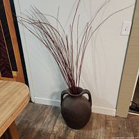Full view of vase with red branches against wall and floor