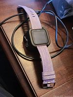 Front view of Fitbit Versa with lavender strap and charger cable