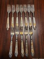 Eight ornate silverplate forks laid side by side