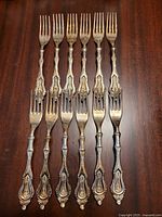 Six ornate silver-plated forks laid out on dark wood surface