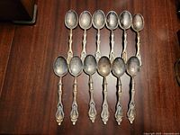 Full set of 12 ornate silverplate spoons on wooden surface