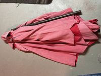 Folded faded red market umbrella with attached black metal pole