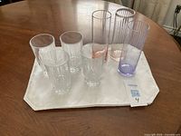 Seven highball glasses displayed on white cloth: four clear crystal-base faceted, three tall coloured ribbed