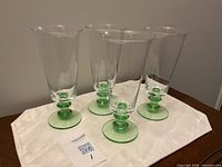 Four clear beer glasses with green stems on white cloth