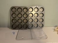 Two 12-cup muffin pans standing side by side with cooling rack in front