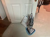 Full view of Hoover steam mop standing upright with attached pad and accessory bag beside it