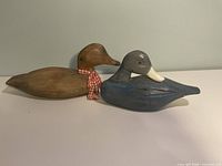 Blue and brown carved wooden duck decoys side by side on white surface