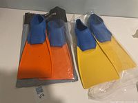 Two pairs Finis swim fins on table; orange and yellow blades visible