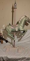 Full view of carved wooden carousel horse on pole and base