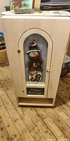 Front view of cream wooden cabinet showing snowman artwork, brass knob, and lower open cubby