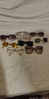 Group shot of eight assorted sunglasses on white surface