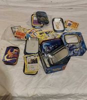 Spread of Pokémon cards, blue lunchbox tin, several mini tins