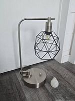 Full view of stainless steel lamp with black cage shade and extra LED bulb