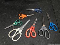 Seven scissors laid out showing sizes and handle colors