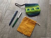Two fountain pens, striped coin purse and mustard pouch laid out