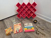overview of lot on floor showing red spice rack, flashbulb boxes, hooks, rods, cup, glass