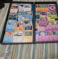 Two trays filled with assorted Pokémon cards from various sets