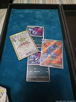 Four sleeved Pokémon cards on blue tray